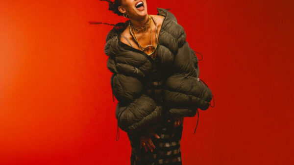 Joyful portrait of a person in a bulky dark green puffer jacket, laughing and dancing against a bright orange background.
