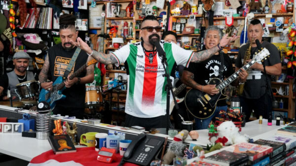 Man with arms outstretched singing into a microphone while a small band plays in a busy toy-and-gift shop behind him